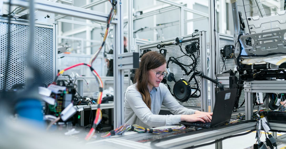 A female engineer focuses on her laptop amidst advanced tech equipment in a lab.